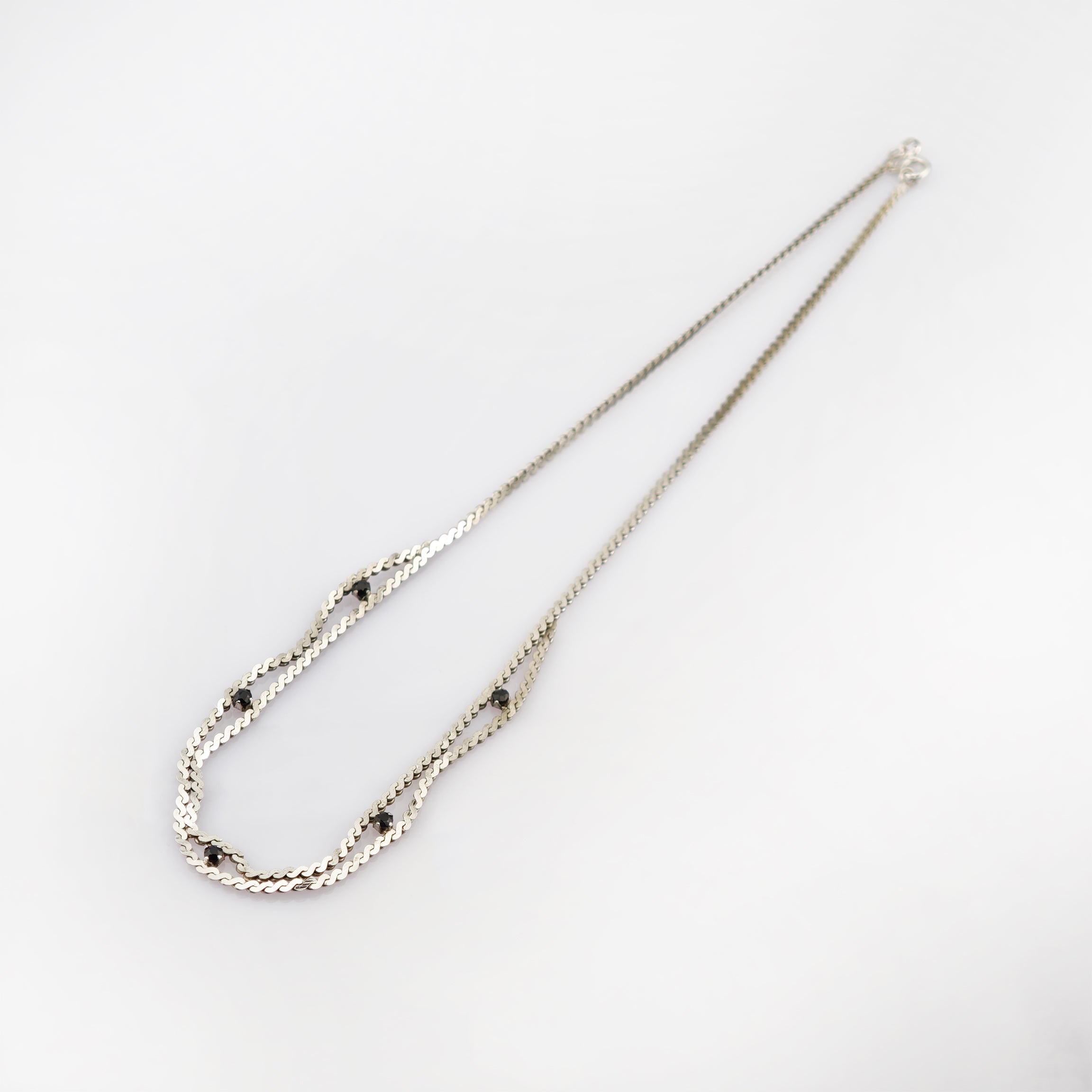 Feine silberne Halskette mit wellenförmiger Gliederung und sechs schwarzen Perlen auf weißem Hintergrund.