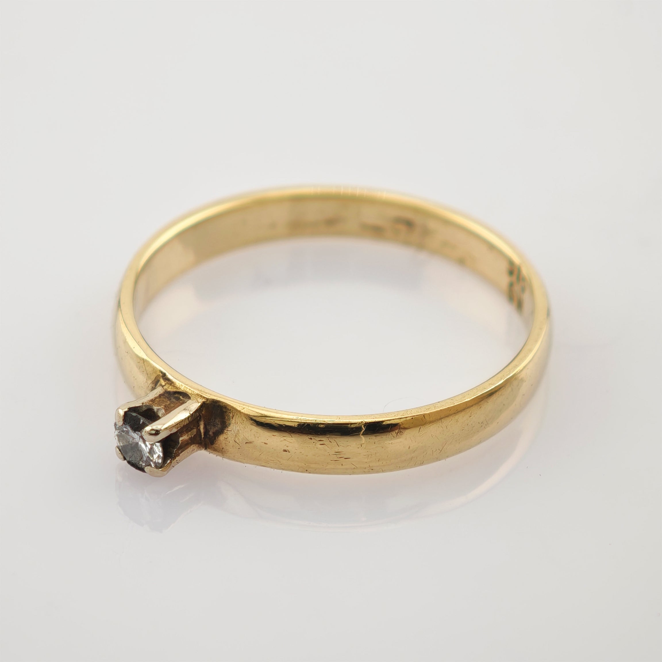 Feiner goldener Ring mit kleinem rundem Diamant in Krappenfassung auf grauem Untergrund.