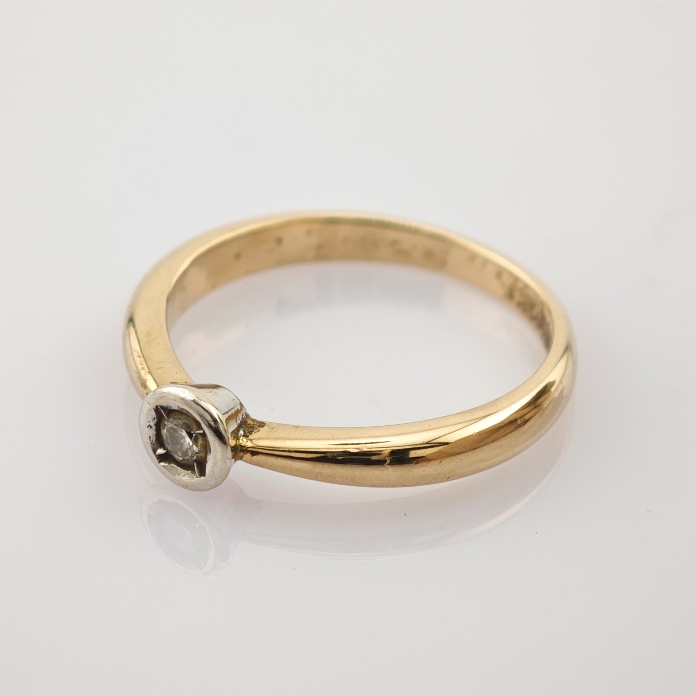 Feiner Goldring mit kleinem rundem Diamanten in silberner Fassung auf weißem Hintergrund