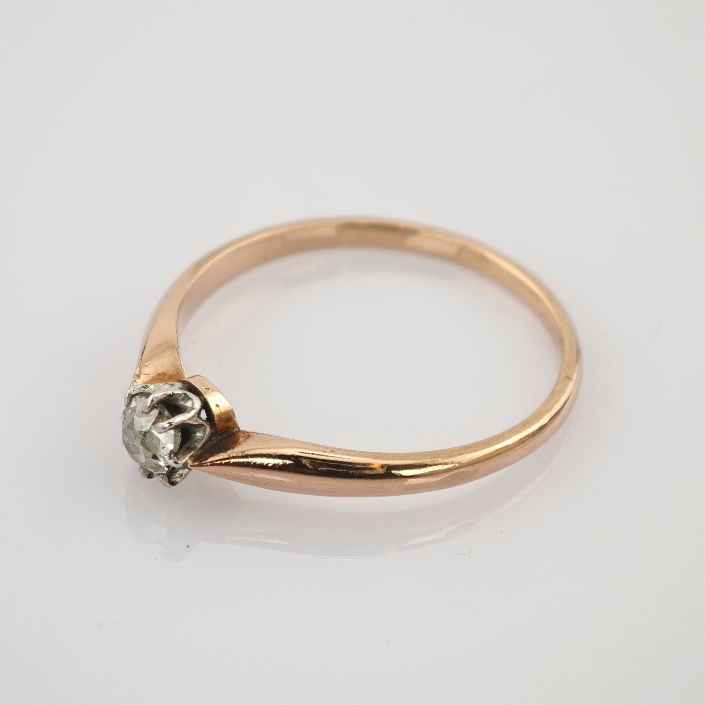 Feiner Goldring mit kleinem Diamant in Silberfassung auf reflektierender weißer Oberfläche