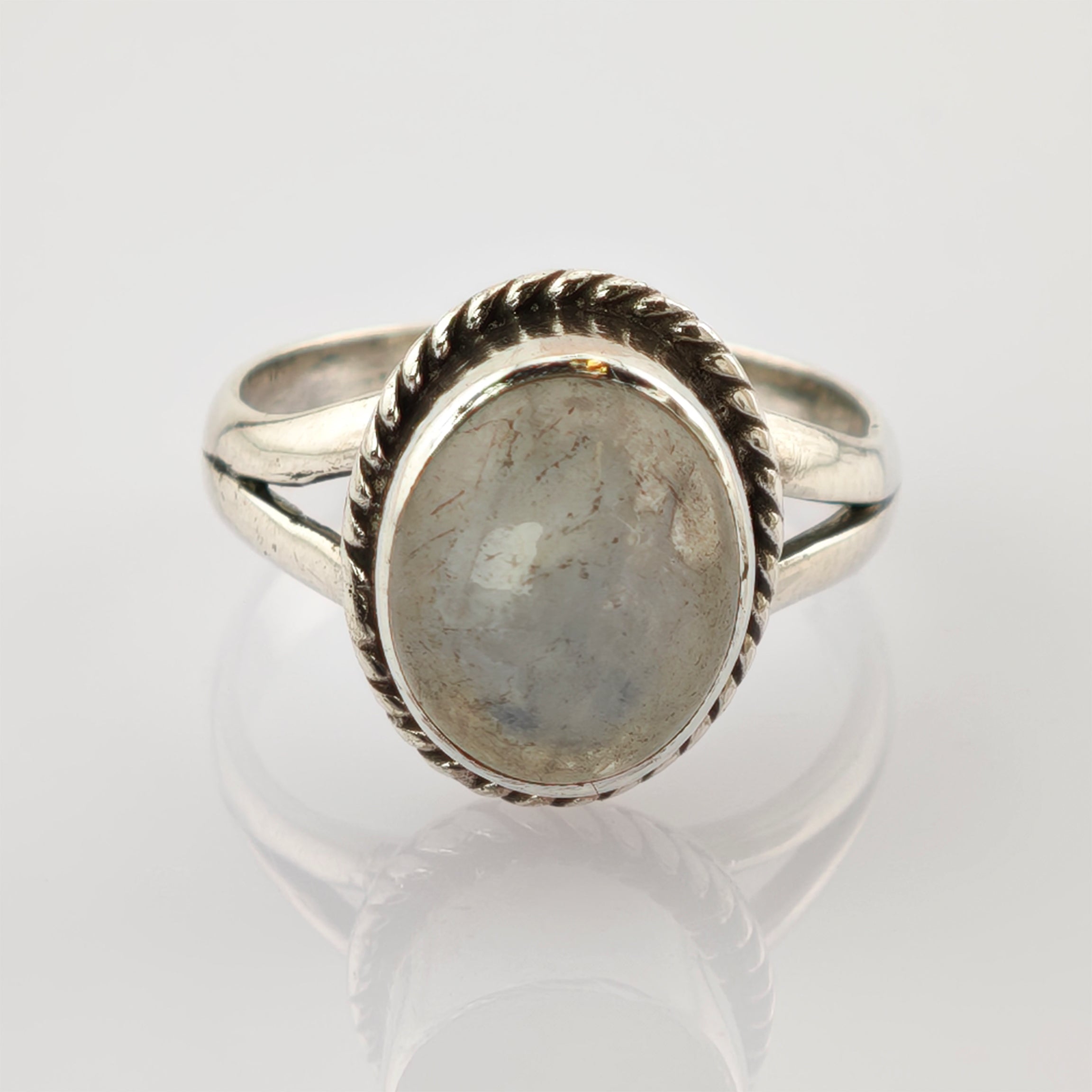 Detaillierter Silberring mit geteiltem Ringband auf reflektierender weißer Oberfläche.