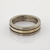 Zweiseitiger Metallring mit silbernem Außenband und goldenem Innenband auf reflektierender Oberfläche