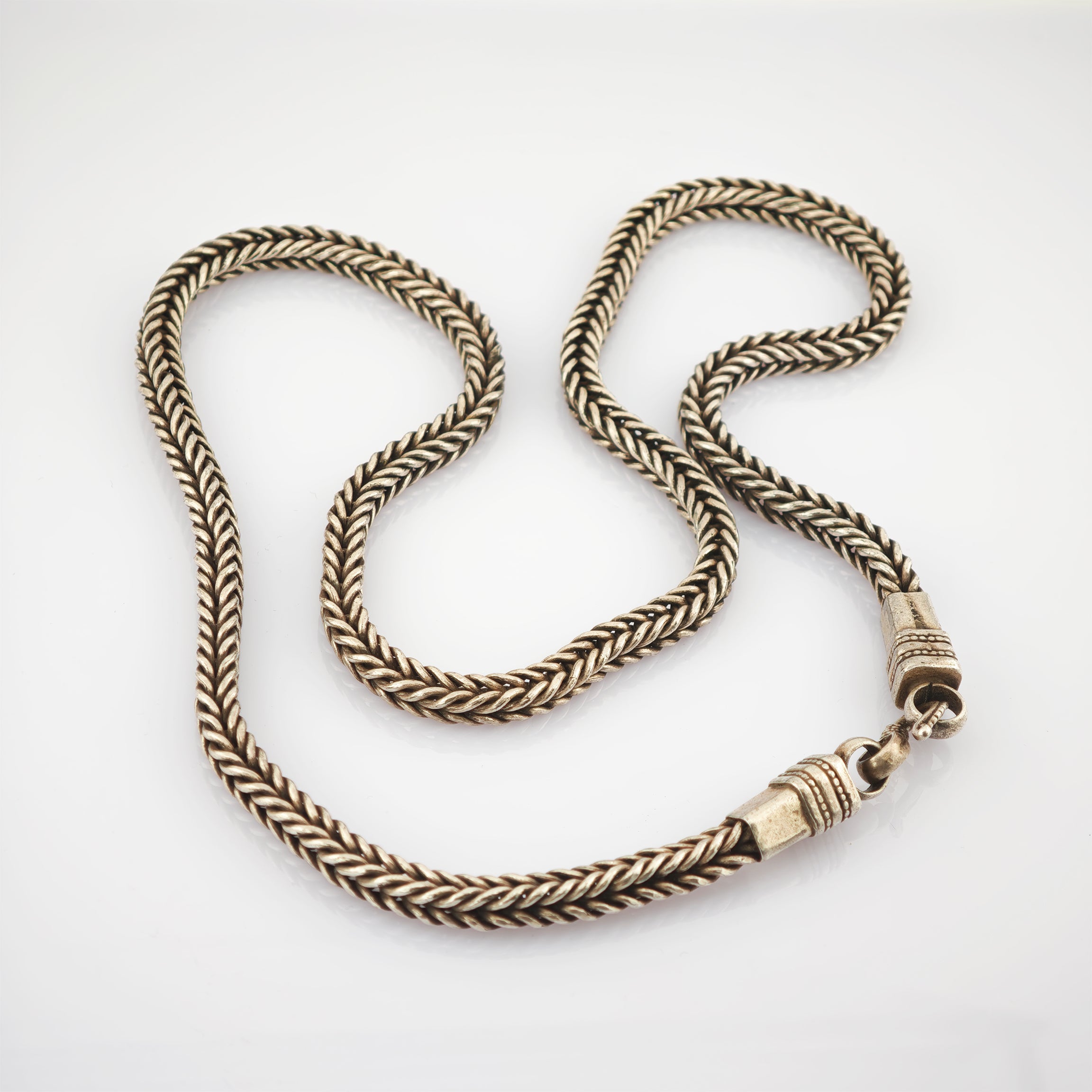 Geschwungene geflochtene Metallkette in gold-bronze auf weißem Hintergrund.