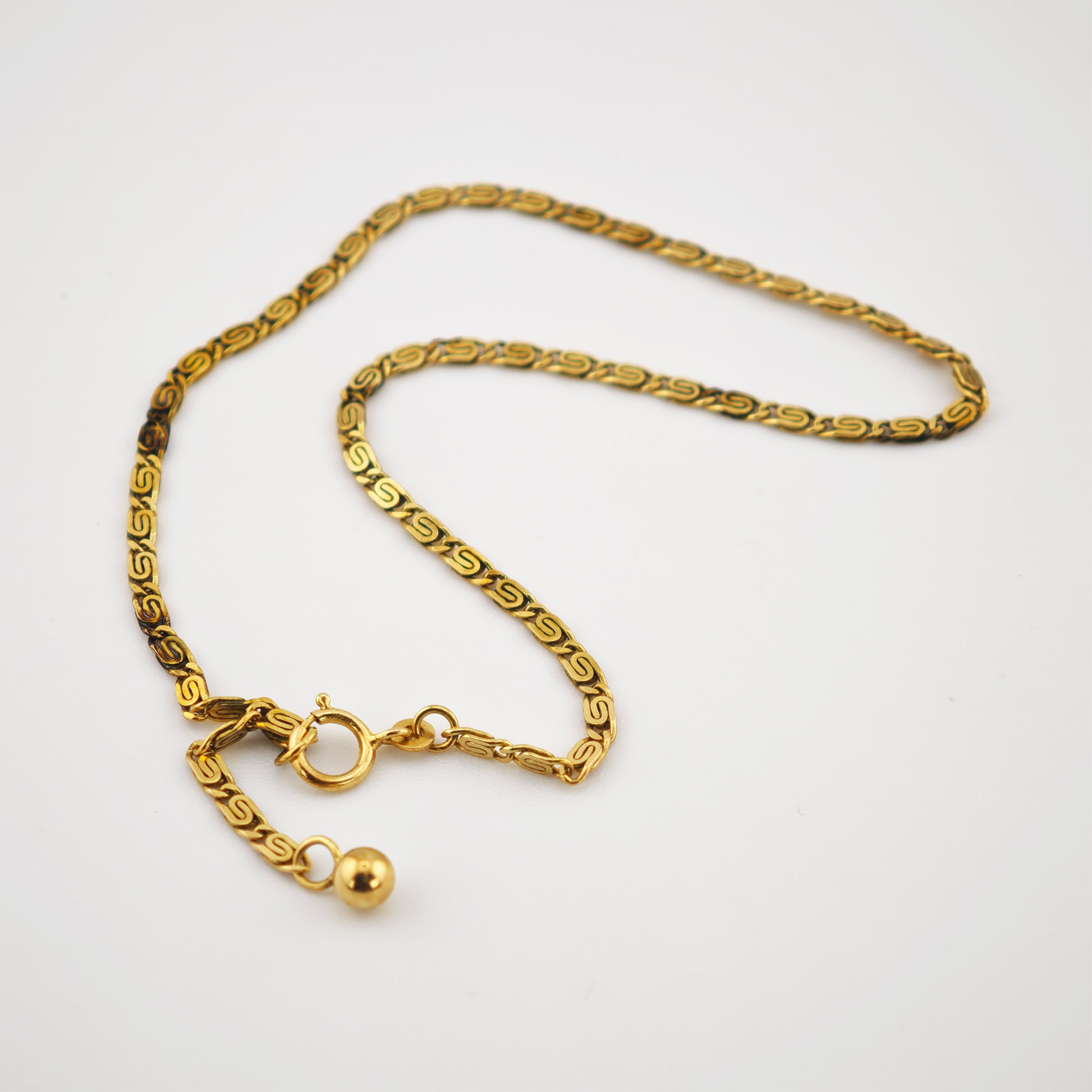 Goldene Halskette mit S-Muster und schwarzen Akzenten, mit Federringverschluss und Perlenende.