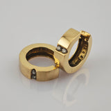 Zwei goldene Ringe mit flachem Band und kleinen Diamanten auf spiegelnder Oberfläche.