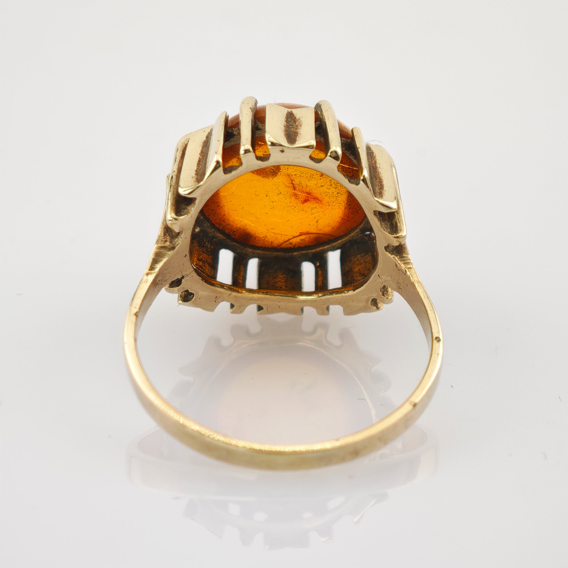 Goldener Ring mit Bernstein in warmem Orange auf weißem reflektierendem Untergrund
