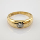 Goldener Ring mit rundem Band und Einzel-Diamanten auf reflektierender weißer Oberfläche