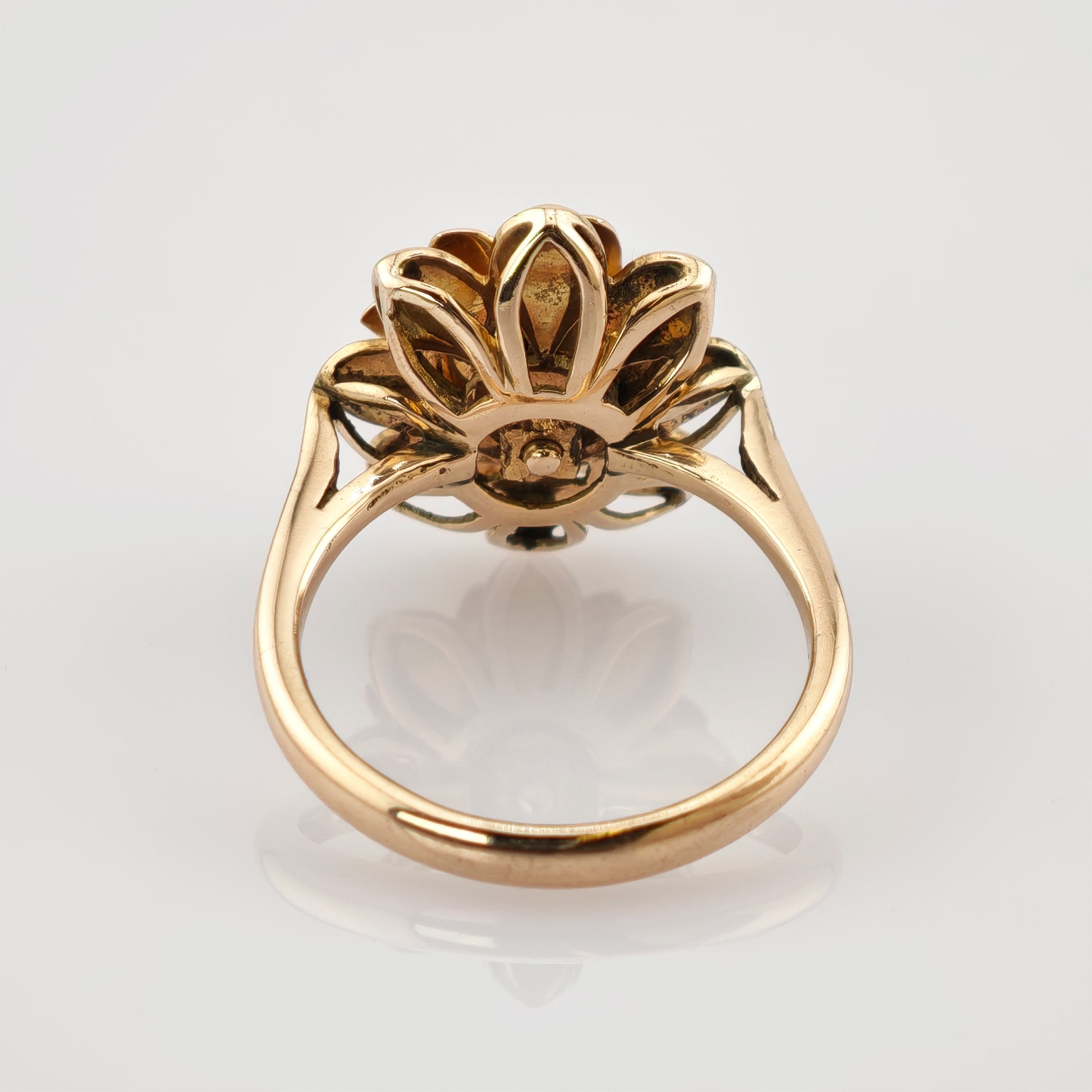 Goldener Ring mit floralem Design und Spiegelung auf reflektierender Oberfläche.