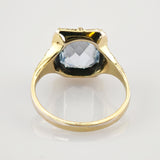 Goldener Ring mit facettiertem hellblauem Edelstein auf reflektierender Oberfläche im Vintage-Stil
