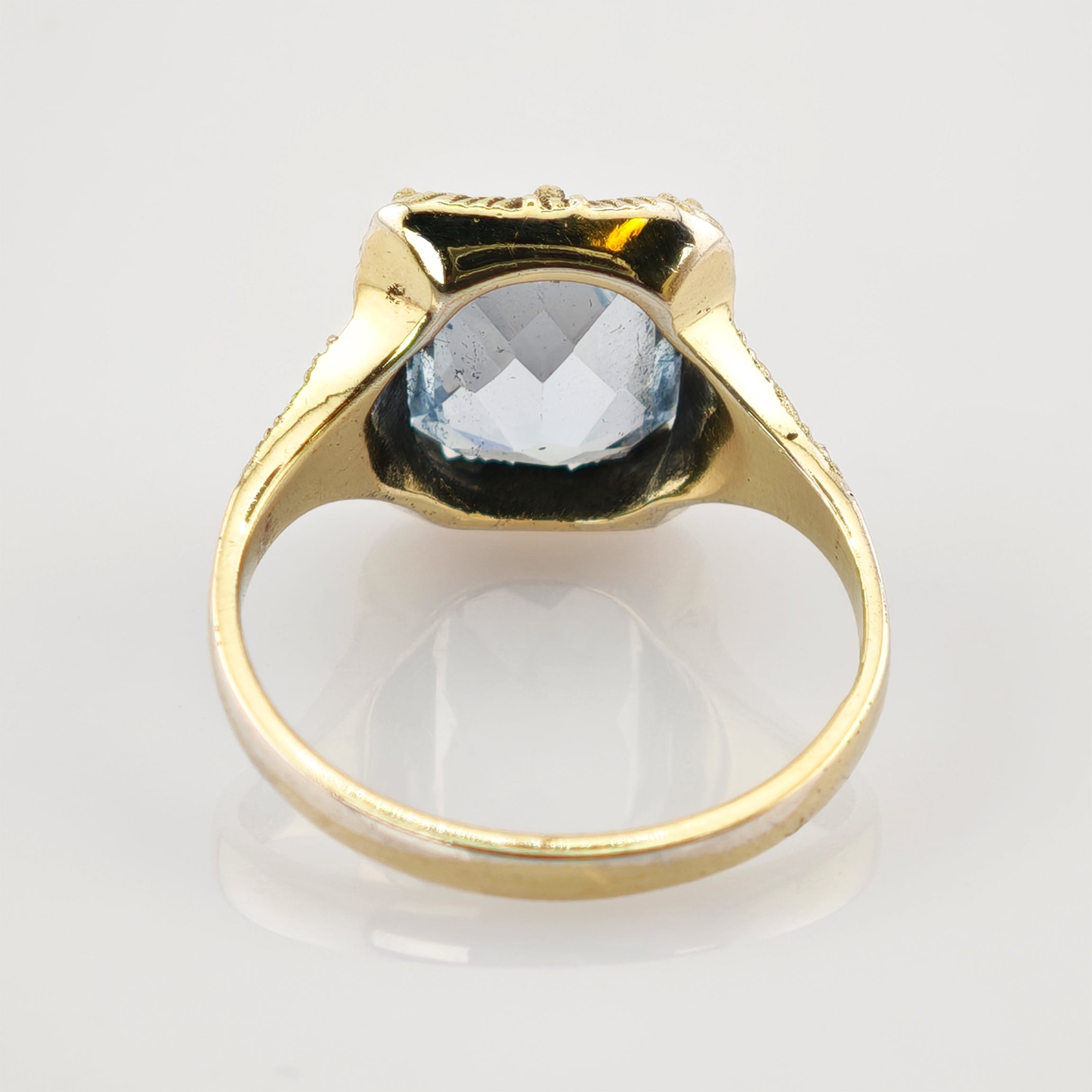 Goldener Ring mit facettiertem hellblauem Edelstein auf reflektierender Oberfläche im Vintage-Stil