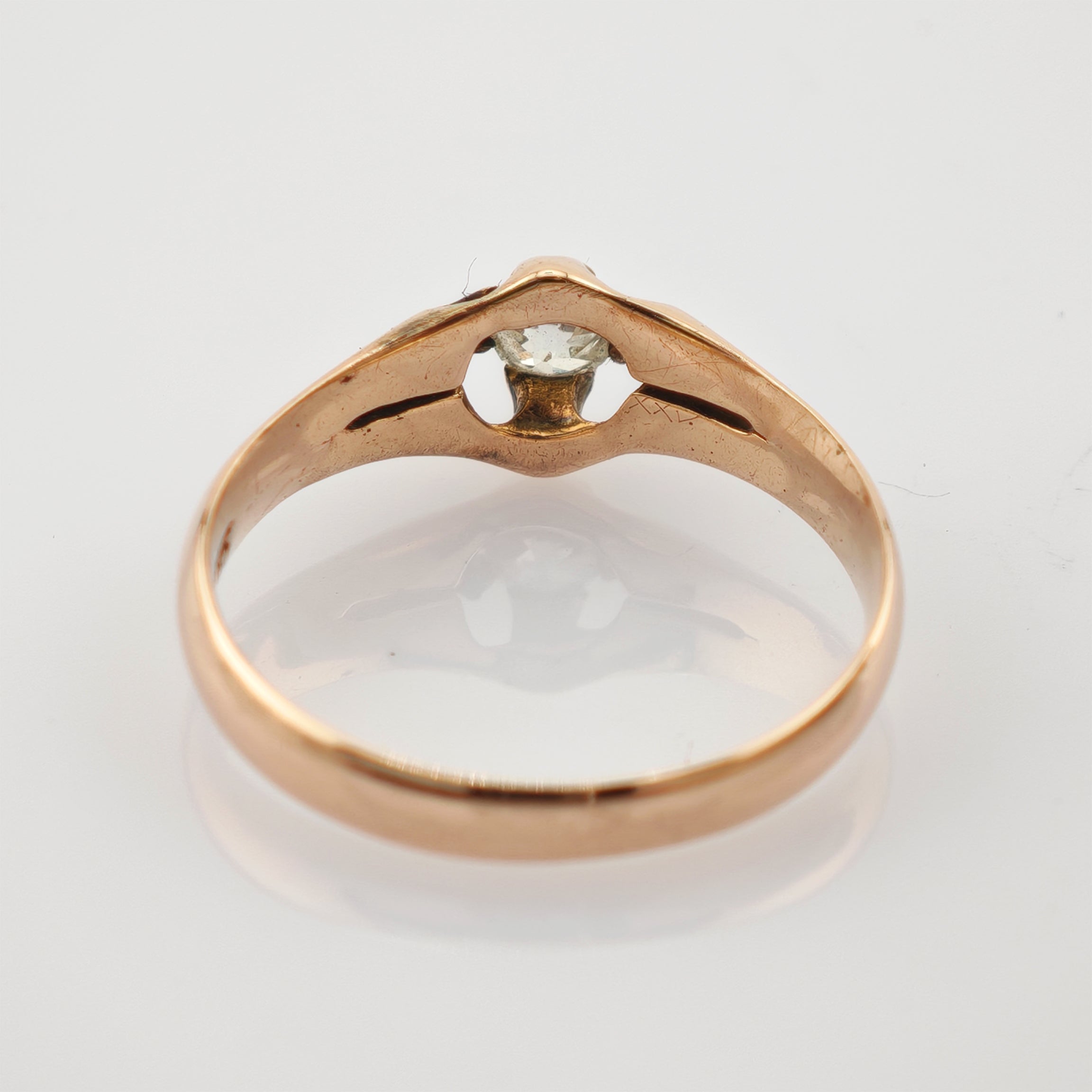 Nahaufnahme eines goldenen Rings mit klarem Edelstein in Krappenfassung auf weißem Hintergrund.