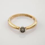 Goldener Ring mit glatter, abgerundeter Bandschiene und kleinem Diamant in Weißmetallfassung auf weißem Hintergrund.