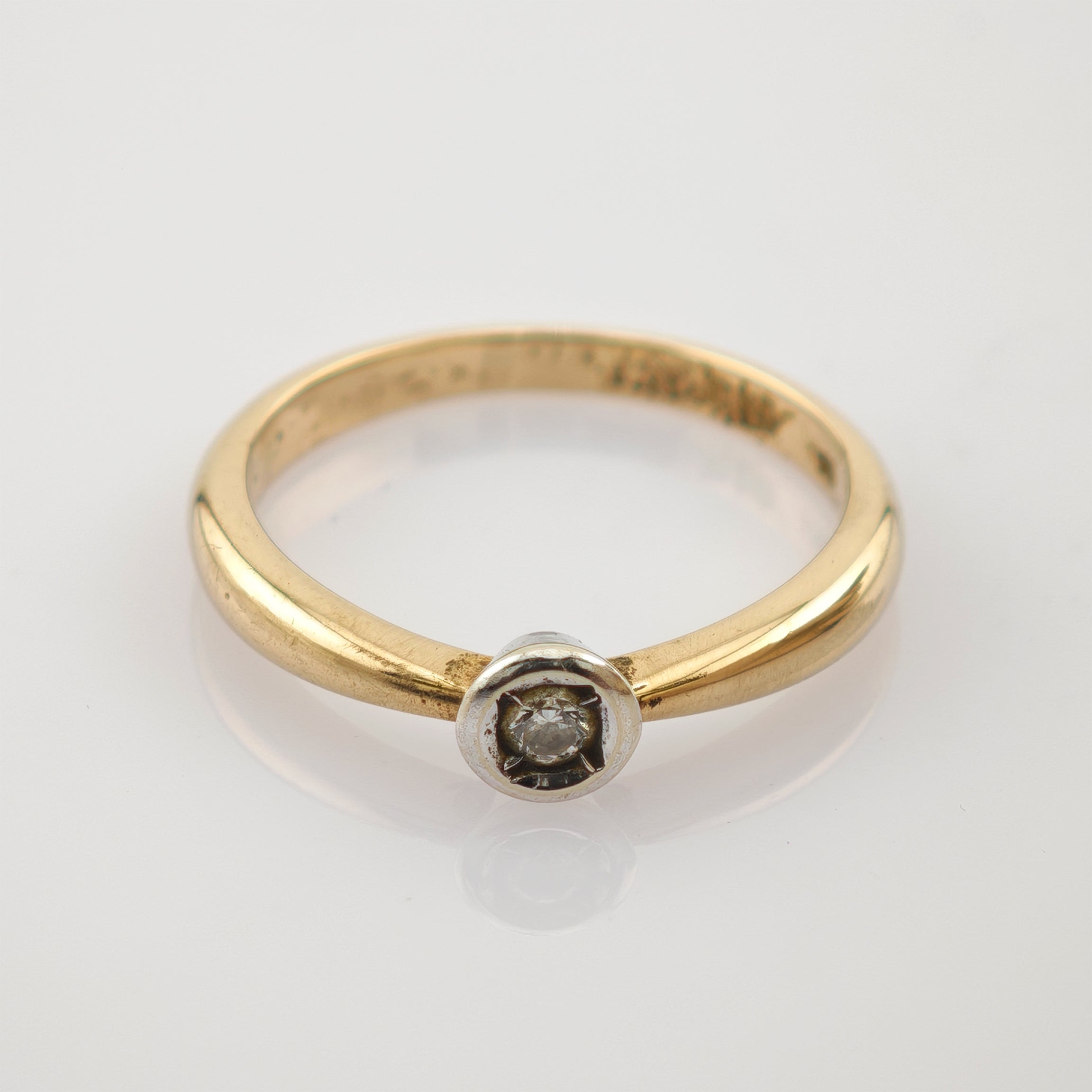 Goldener Ring mit glatter, abgerundeter Bandschiene und kleinem Diamant in Weißmetallfassung auf weißem Hintergrund.