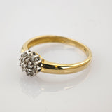 Nahaufnahme eines goldenen Rings mit einem silbernen Diamantcluster auf weißem reflektierendem Untergrund.