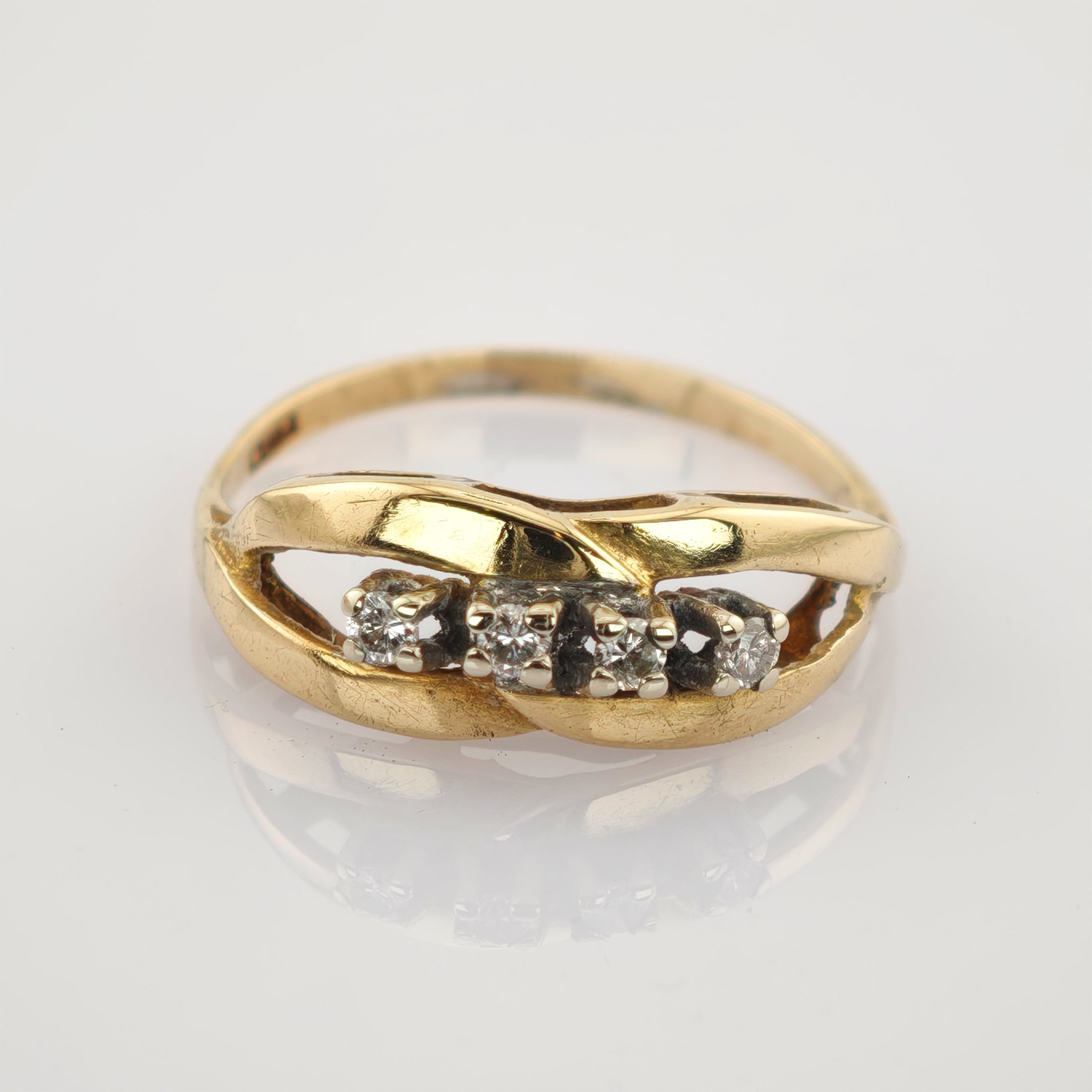 Goldener Ring mit verdrehtem Band und vier kleinen Diamanten auf hellem Hintergrund.
