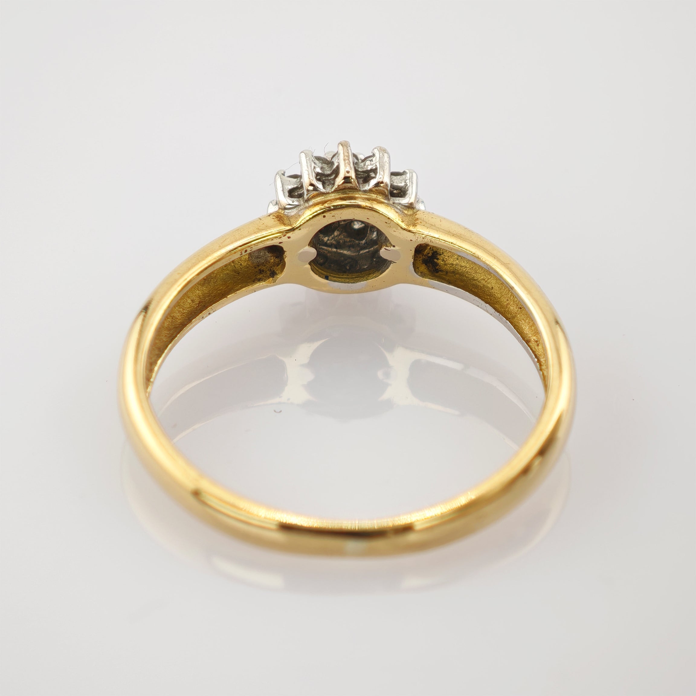 Goldener Ring mit vier weißen Steinen auf polierter Oberfläche.