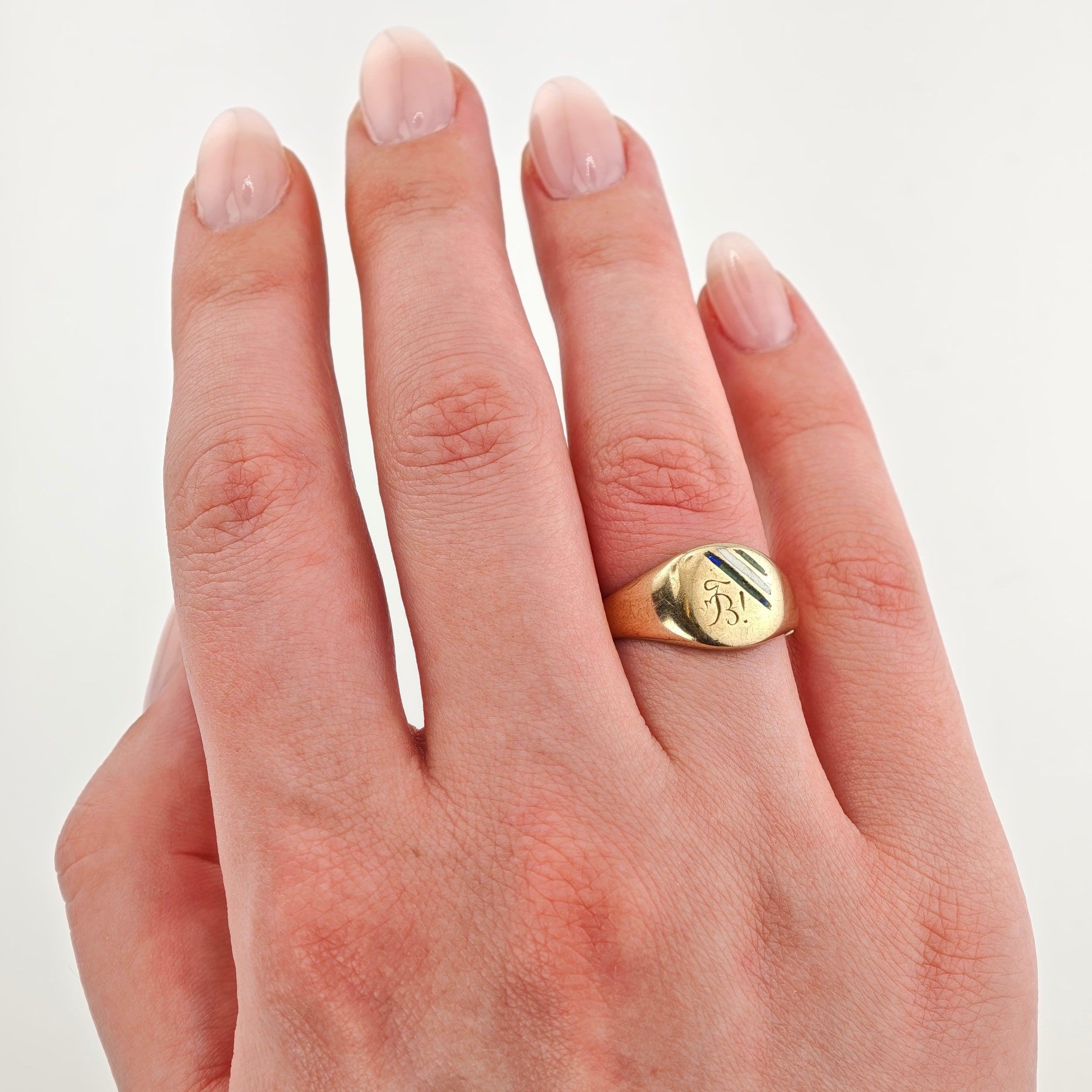 Goldener Siegelring mit eingraviertem B und blauen sowie schwarzen Emaille-Diagonallinien am linken Ringfinger