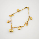 Feines goldfarbenes Armband mit Kette und kleinen herzförmigen Anhängern auf weißem Hintergrund.
