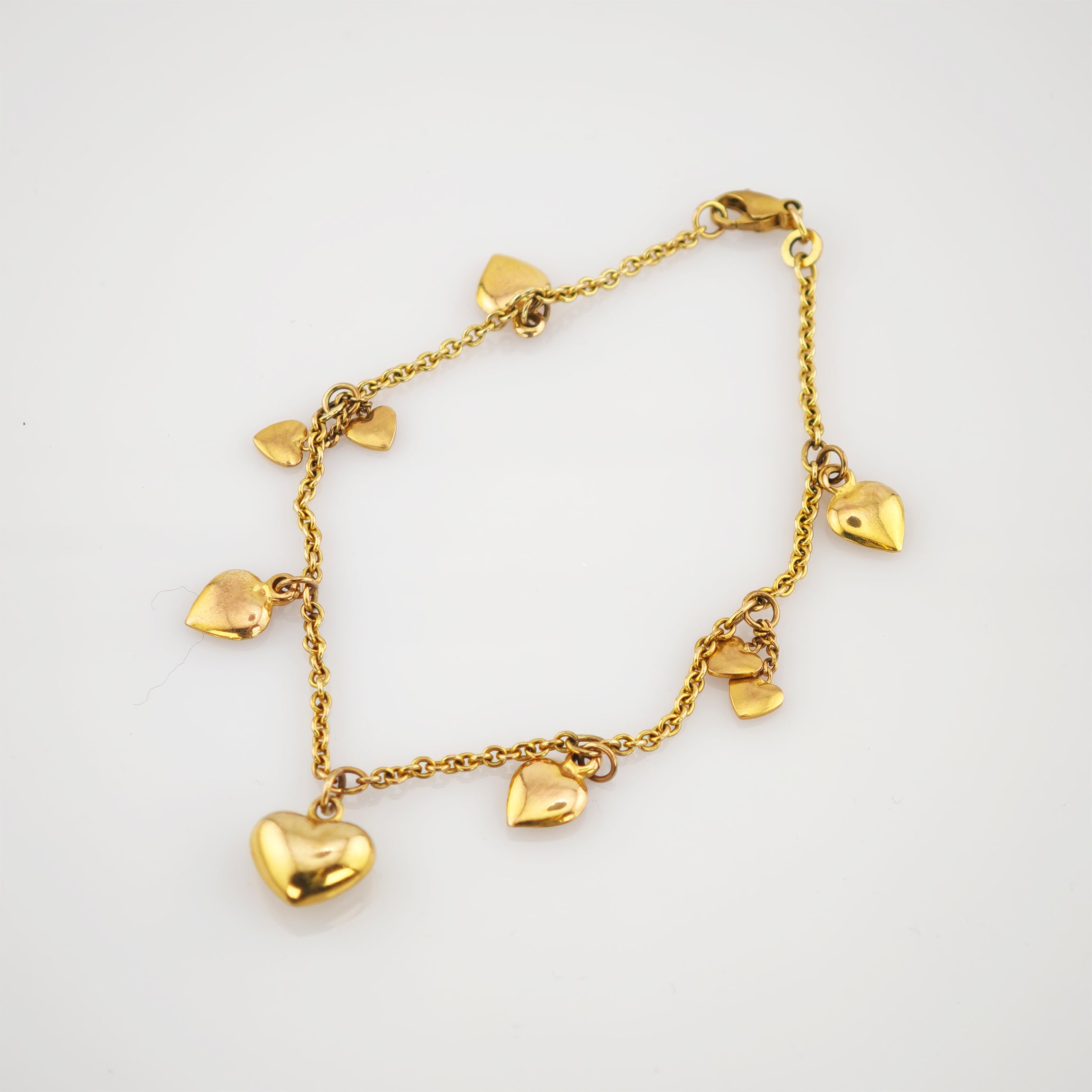 Feines goldfarbenes Armband mit Kette und kleinen herzförmigen Anhängern auf weißem Hintergrund.