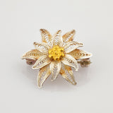 Goldfarbene Brosche in Form einer achtblättrigen Blume mit Netzmuster und strukturiertem Zentrum im Vintage-Stil.