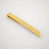 Goldfarbene Krawattenklammer mit strukturierter Oberfläche und rechteckiger Form auf reflektierendem Hintergrund