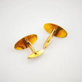 Ein Paar goldfarbene Manschettenknöpfe mit ovalen Gesichtern und Scharniermechanismus auf weißem Hintergrund.