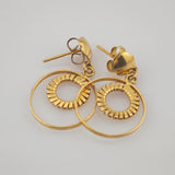 Goldfarbene Ohrstecker mit kleinen, kreisförmigen Ringen und Schmetterlingsverschlüssen auf hellem Untergrund.