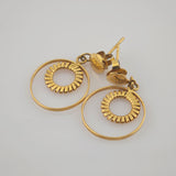 Paar goldfarbener Vintage-Ohrringe mit kreisförmigem Design und strukturierten inneren Ringen auf hellem Hintergrund.