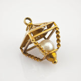 Goldfarbener Anhänger mit gedrehten Drahtkanten und zentraler weißer Perle in geometrischem Rahmen.