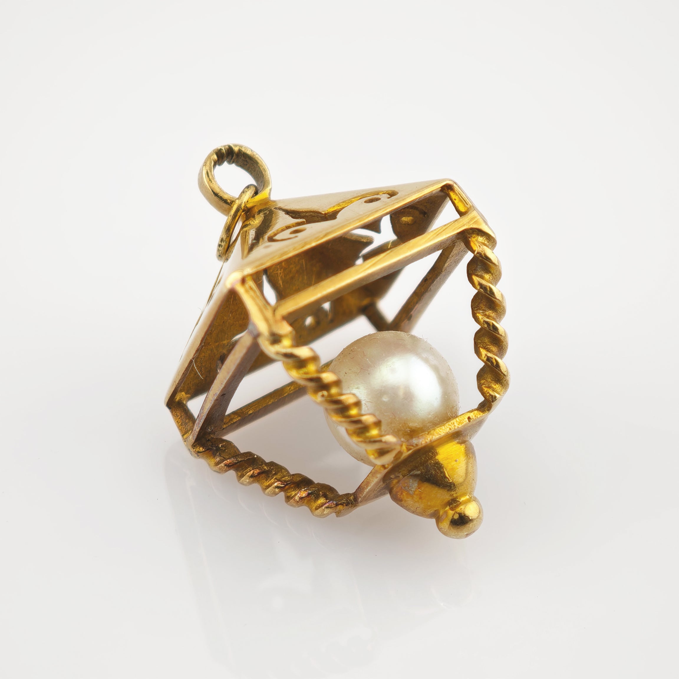 Goldfarbener Anhänger mit gedrehten Drahtkanten und zentraler weißer Perle in geometrischem Rahmen.