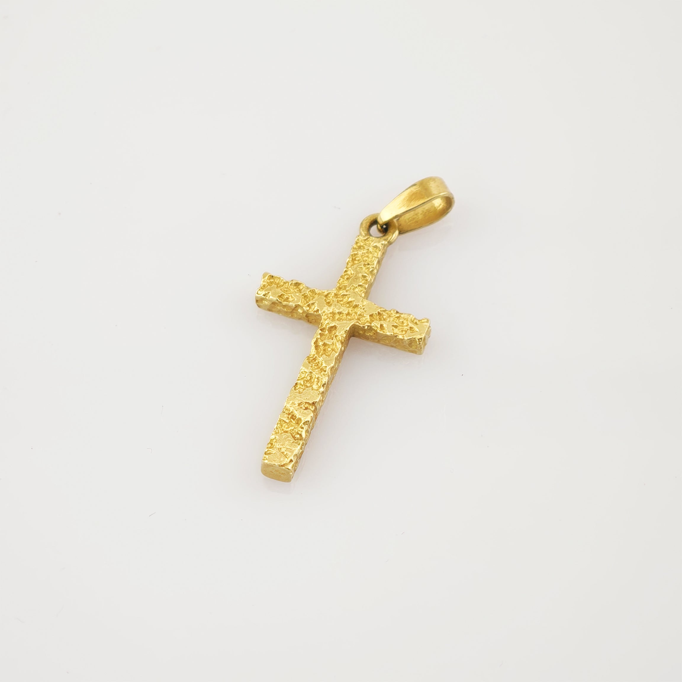 Goldfarbener Kreuzanhänger mit strukturierter, unebener Oberfläche auf weißem Hintergrund.