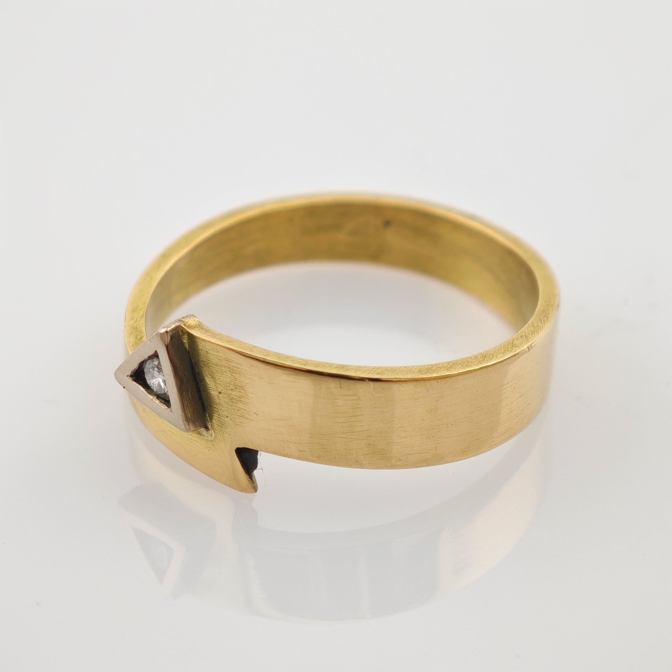 Goldfarbener Ring mit flacher Ringschiene und dreieckigem Designelement mit klarem Edelstein.