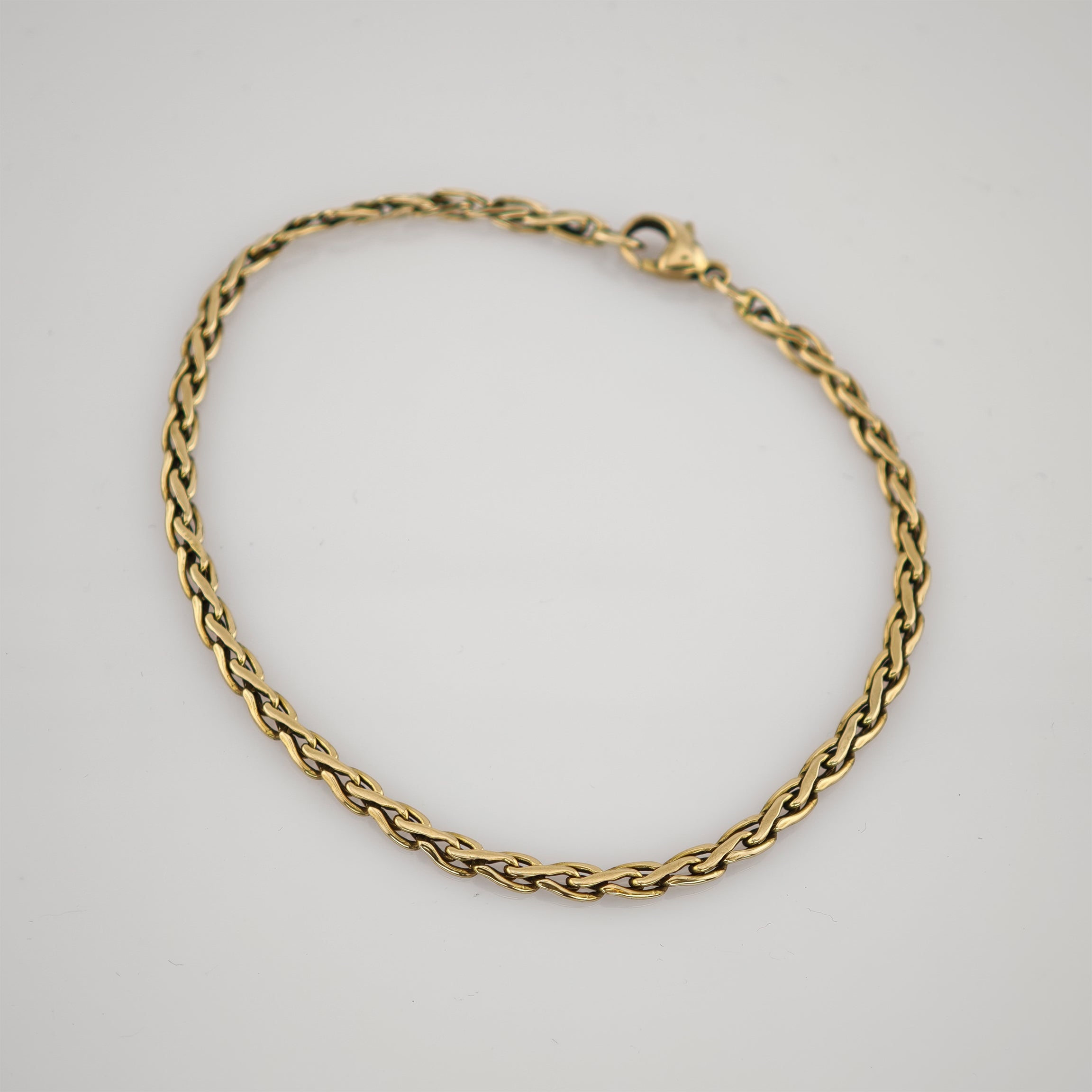 Goldfarbenes gedrehtes Seilarmband aus poliertem Metall mit Karabinerverschluss auf weißem Hintergrund.