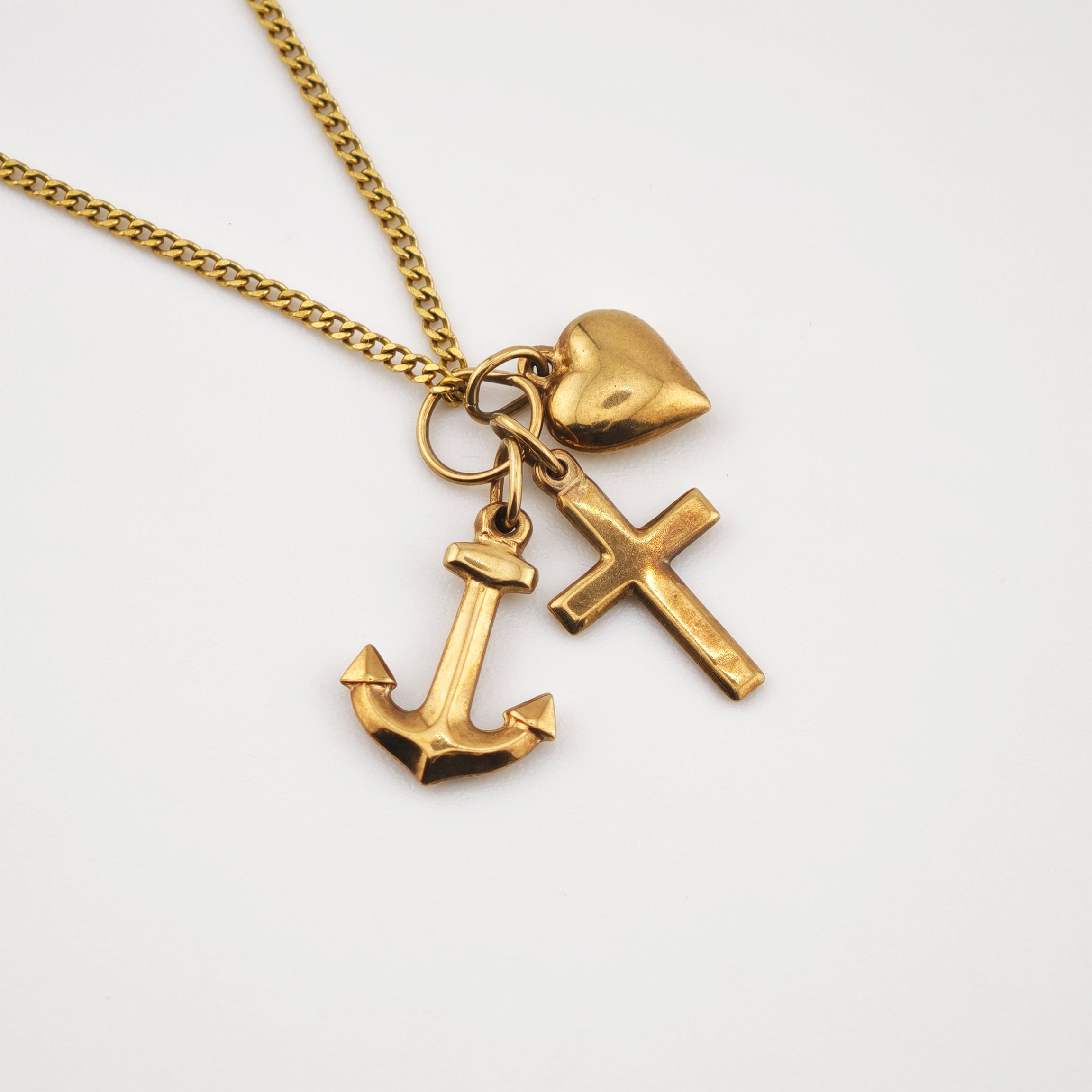 Goldkette mit Herz-, Kreuz- und Ankeranhängern auf weißem Hintergrund
