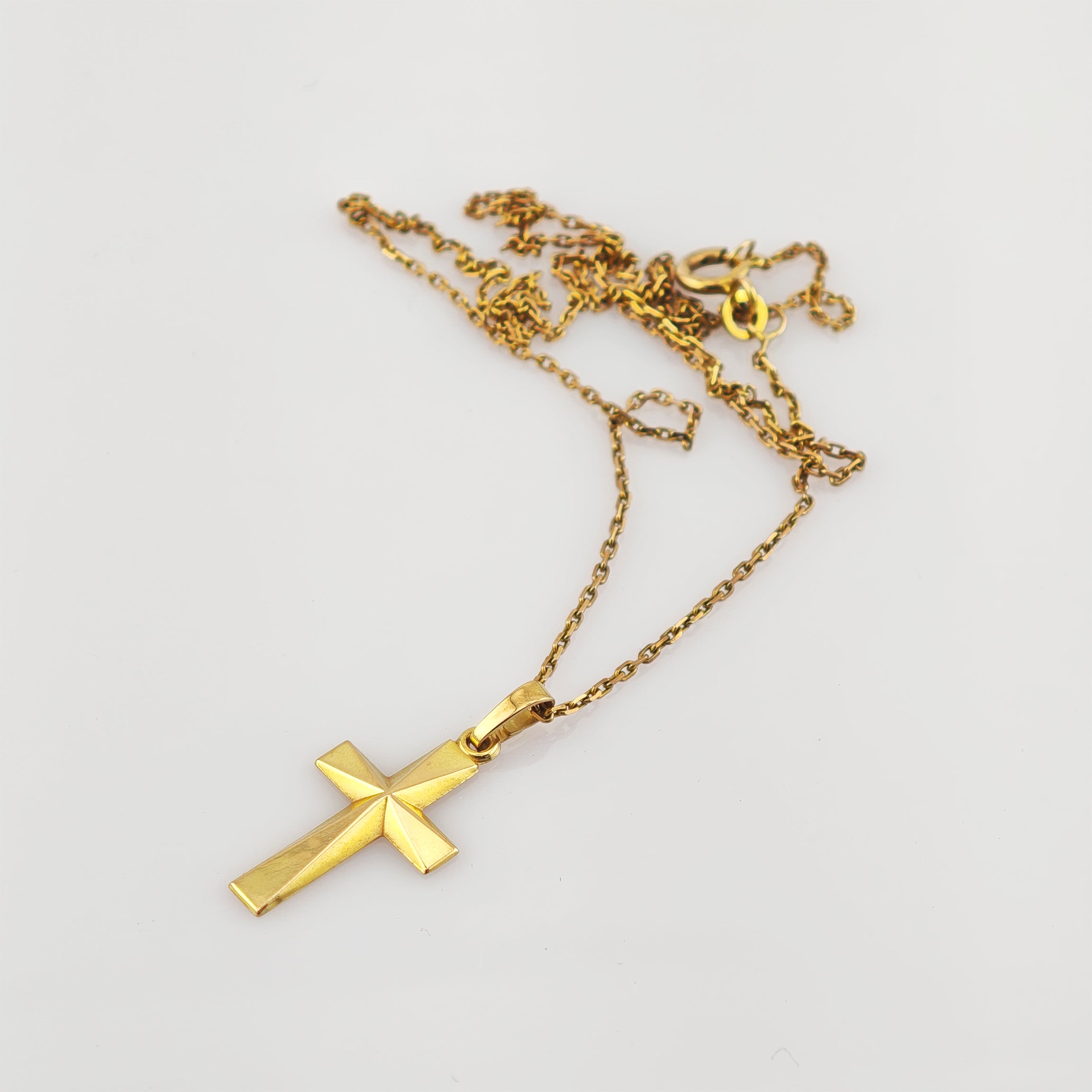 Goldfarbener Kreuzanhänger mit geometrischem Reliefmuster an feiner Kette auf weißem Hintergrund.