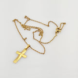 Goldkreuzanhänger mit glatter, facettierter Oberfläche an zarter Goldkette auf weißem Hintergrund