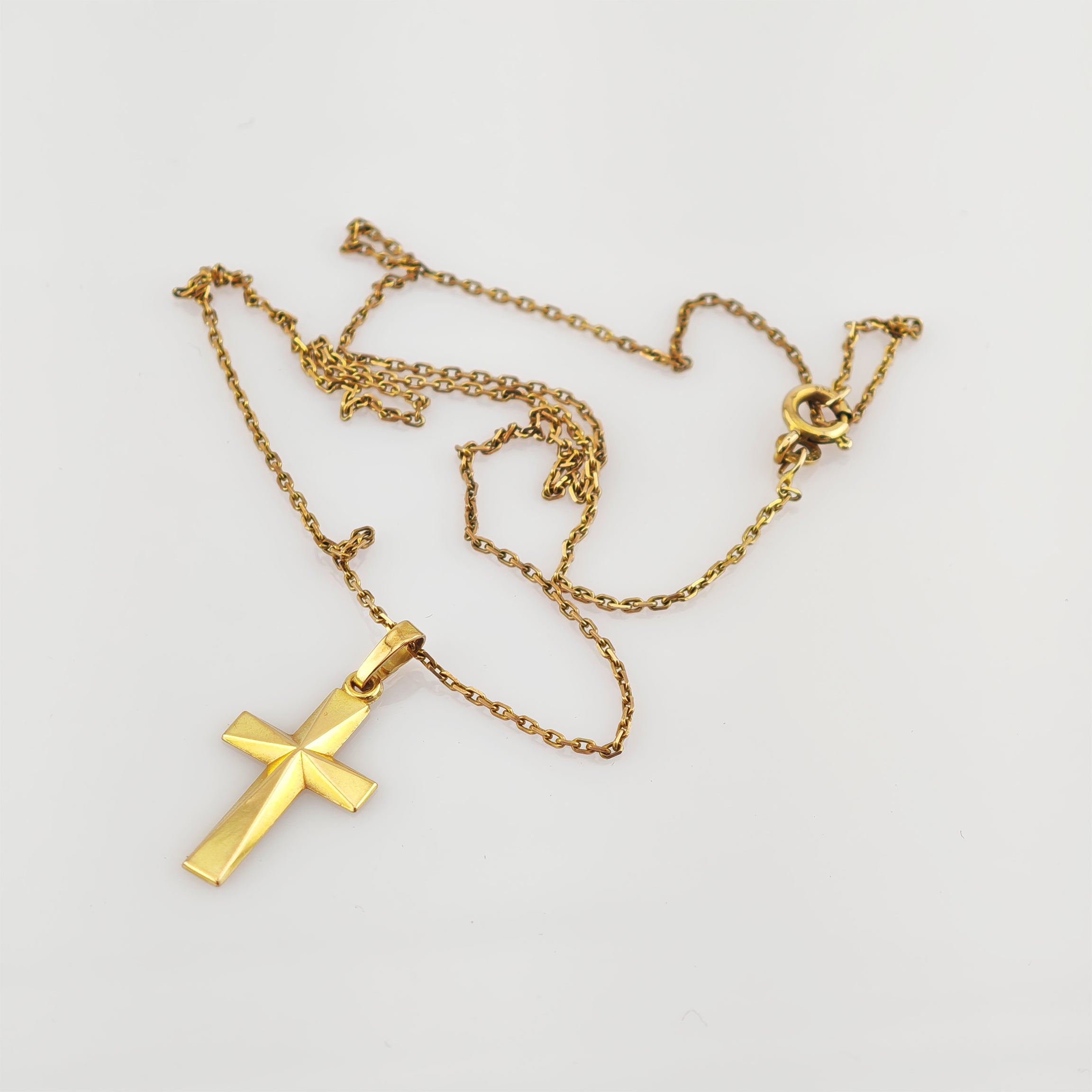 Goldkreuzanhänger mit glatter, facettierter Oberfläche an zarter Goldkette auf weißem Hintergrund