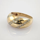 Goldring mit gewölbtem Band, diagonalen silbernen Einlagen und funkelnden Steinen auf hellem Hintergrund.