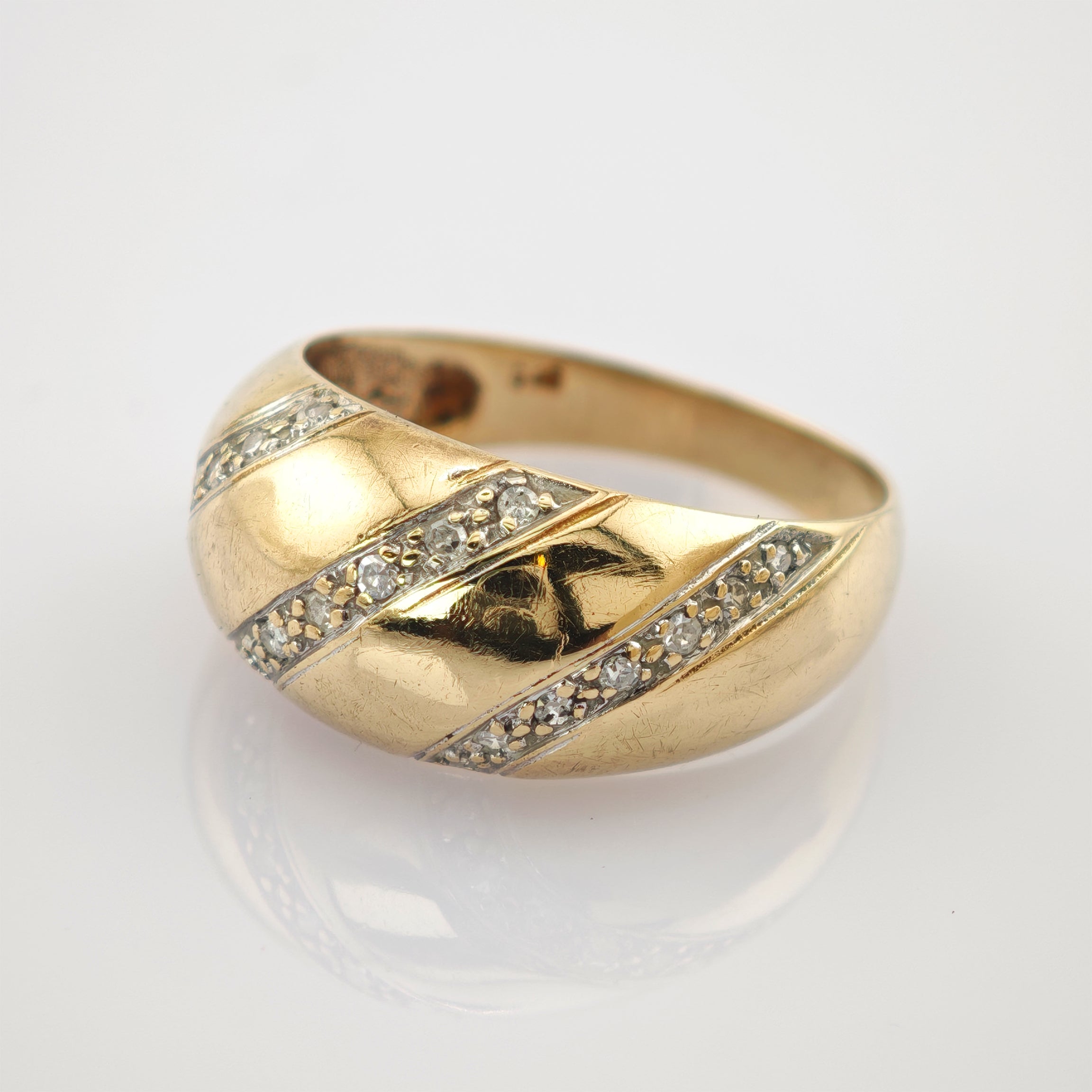 Goldring mit gewölbtem Band, diagonalen silbernen Einlagen und funkelnden Steinen auf hellem Hintergrund.