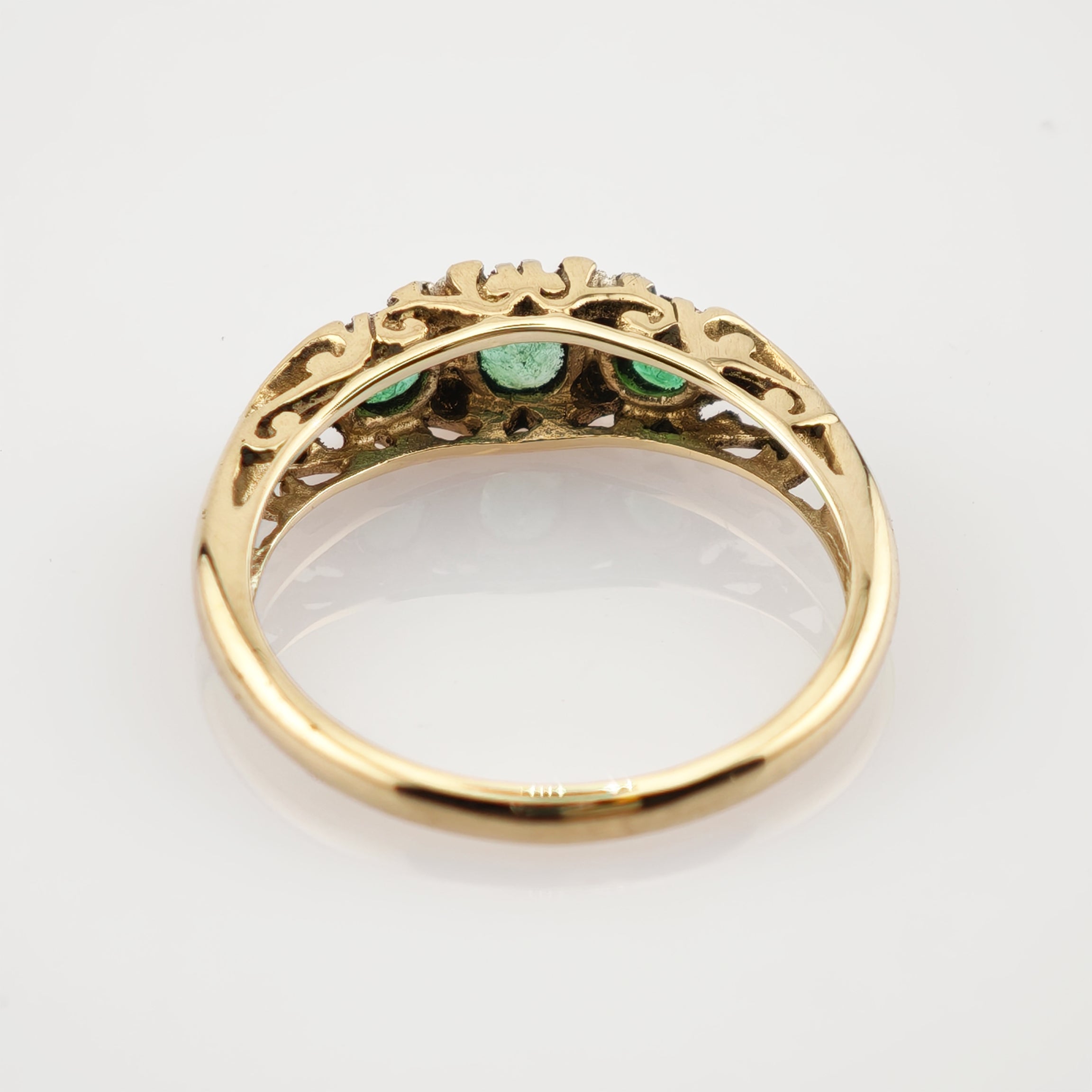 Goldring mit filigraner Offenarbeit und drei grünen Steinen auf weißem Hintergrund