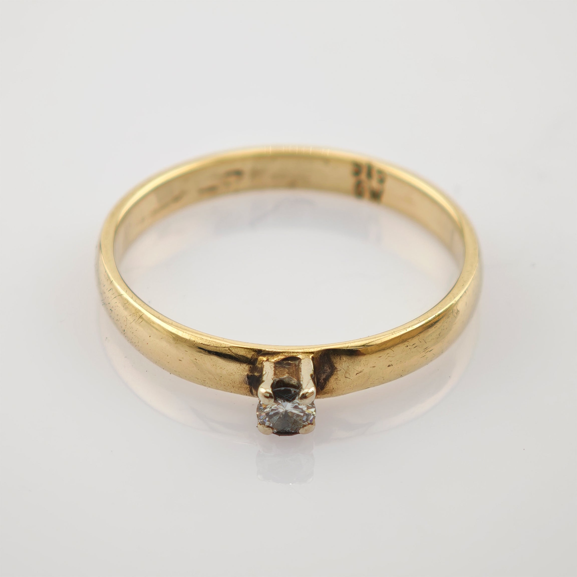 Goldring mit schmalem Band und kleinem rundem klaren Edelstein in Vier-Krappen-Fassung.