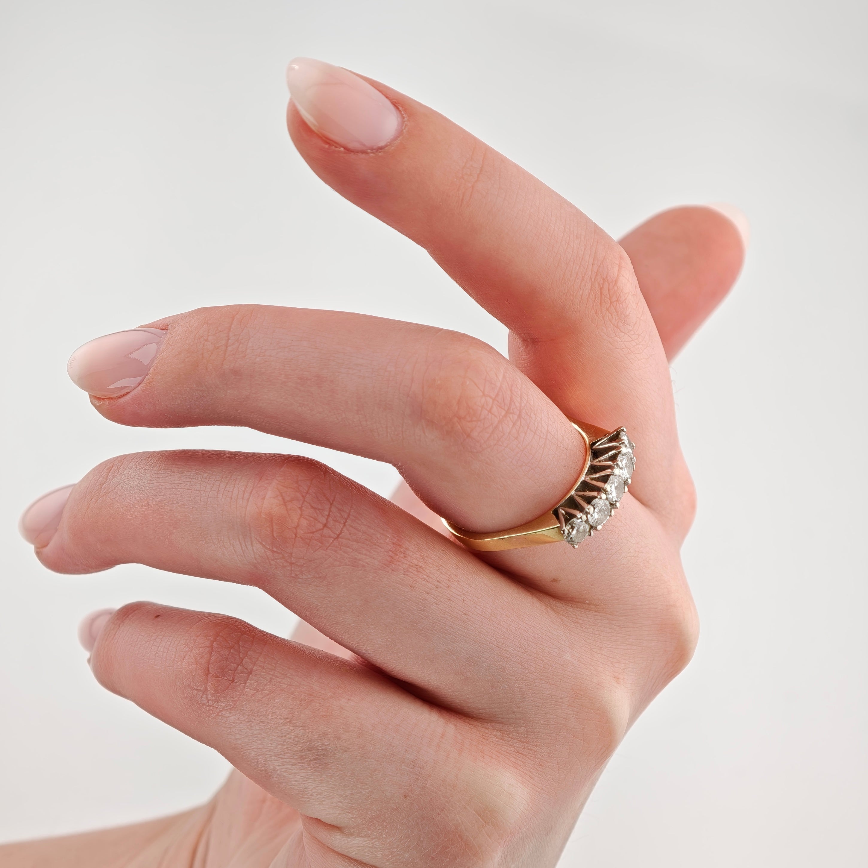 Hand mit elegantem Goldring besetzt mit fünf runden weißen Diamanten vor hellem Hintergrund.