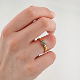 Hand mit Goldring am Ringfinger mit floralem Diamantcluster vor weißem Hintergrund