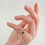 Hand mit elegantem Goldring am Zeigefinger, breiter Ring mit Diamant vor hellem Hintergrund.