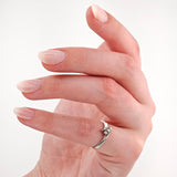 Nahaufnahme einer Hand mit hellrosa lackierten Nägeln und einem silbernen Ring mit Edelsteinen am Ringfinger.