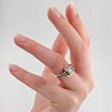 Hand mit langen, mandelförmigen Nägeln in rosa Nude und silbernem Ring mit klarem Edelstein vor grauem Hintergrund