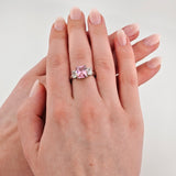 Hand mit gepflegten, rosa lackierten Nägeln und Ring mit rosa Edelstein und klaren Steinen