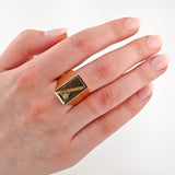 Hand mit gepflegten, rosa lackierten Nägeln mit geometrischem goldfarbenem Ring und kleinem klaren Edelstein