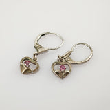 Kleine Silberohrringe mit herzförmigen Anhängern und roten Edelsteinen auf hellem Hintergrund