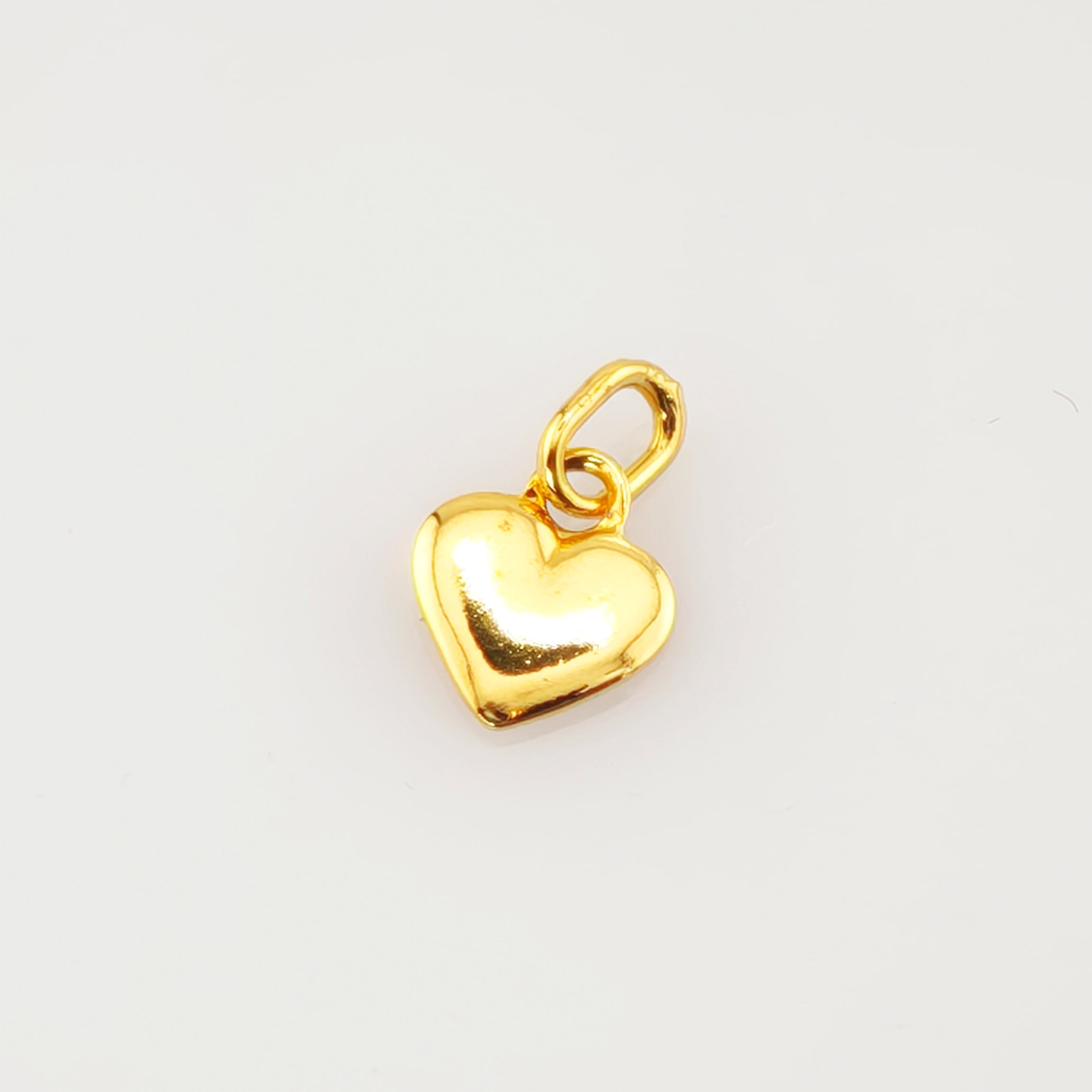 Kleiner glänzender goldener Herzanhänger mit Schlaufe auf weißem Hintergrund.